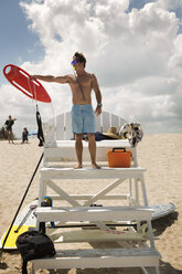 Man holding buoy while standing on lifeguard chair - CAVF05880