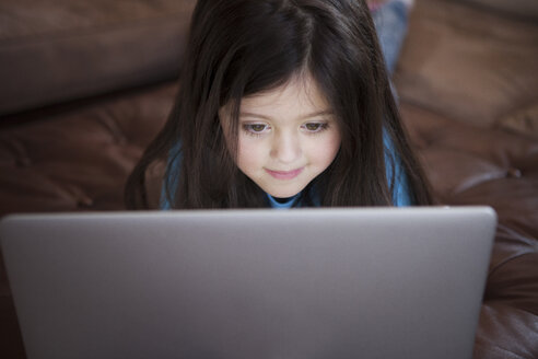 Nettes Mädchen, das einen Laptop benutzt, während es zu Hause liegt - CAVF05921