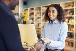 Eine Frau nimmt die Kreditkarte eines Kunden, während sie im Laden steht - CAVF05926