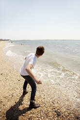 Rückansicht eines Mannes, der einen Stein ins Meer wirft, während er am Ufer steht - CAVF05982