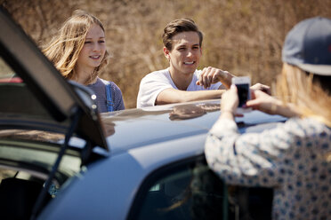 Woman using smart phone while standing with friends by car - CAVF05991