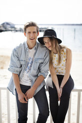 Portrait of couple sitting on railing at pier against beach - CAVF06034