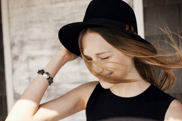 Woman holding sun hat against wooden wall - CAVF06035