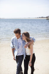 Paar, das sich in den Armen liegt und am Strand spazieren geht - CAVF06036