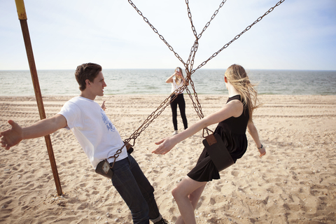 Frau fotografiert Freunde auf einer Schaukel am Strand, lizenzfreies Stockfoto