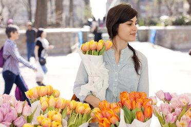 Frau mit Tulpenblüten, die auf dem Blumenmarkt steht und wegschaut - CAVF06059