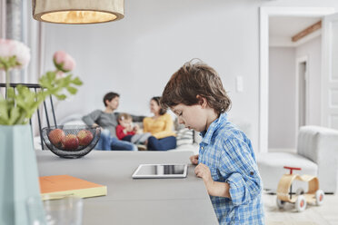 Boy looking at tablet at home with family in background - RORF01123