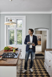 Man using tablet in kitchen looking at ceiling lamp - RORF01124