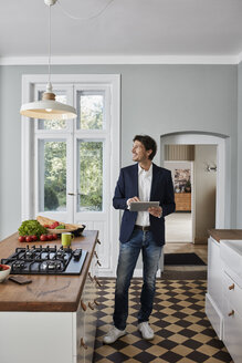 Mann benutzt Tablet in der Küche und schaut auf die Deckenlampe - RORF01124