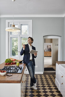 Man using tablet in kitchen looking at ceiling lamp - RORF01125