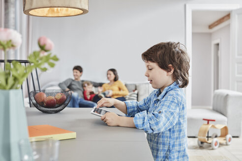 Junge schaut auf Tablet zu Hause mit Familie im Hintergrund - RORF01126