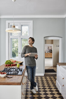 Man using tablet in kitchen looking at ceiling lamp - RORF01127