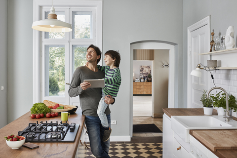 Father and son using tablet in kitchen looking at ceiling lamp stock photo