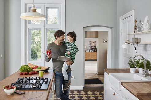 Happy father and son with bell pepper and tablet in kitchen - RORF01133