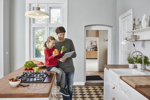 Lächelnder Vater und Tochter mit Paprika und Tablet in der Küche - RORF01135