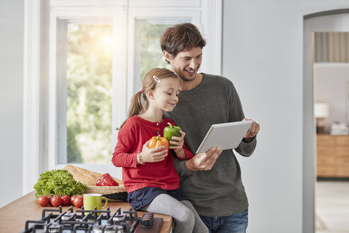 Lächelnder Vater und Tochter mit Paprika und Tablet in der Küche - RORF01137