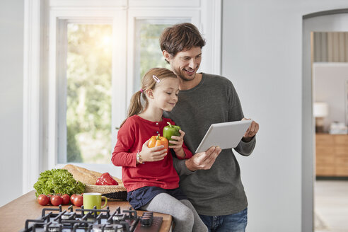 Smiling father and daughter with bell pepper and tablet in kitchen - RORF01137