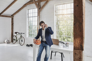 Smiling businessman with basketball on cell phone in penthouse - RORF01141