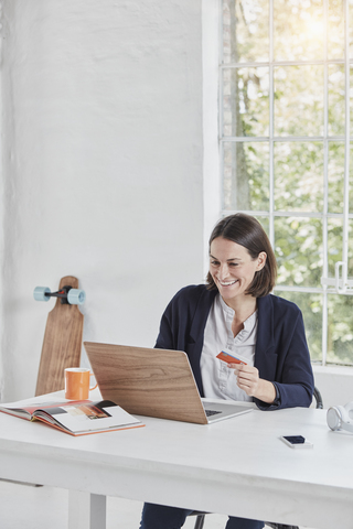 Glückliche Geschäftsfrau mit Laptop auf dem Schreibtisch, die eine Karte hält, lizenzfreies Stockfoto
