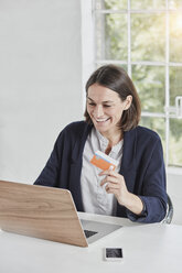Lachende Geschäftsfrau mit Laptop auf dem Schreibtisch, die eine Karte hält - RORF01155