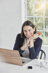 Porträt einer lächelnden Geschäftsfrau mit Laptop auf dem Schreibtisch, die eine Karte hält - RORF01156