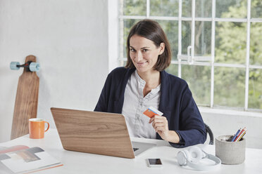 Porträt einer lächelnden Geschäftsfrau mit Laptop auf dem Schreibtisch, die eine Karte hält - RORF01158