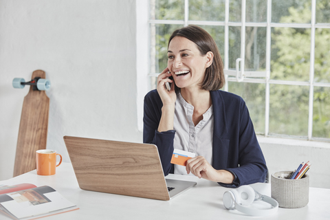 Lachende Geschäftsfrau mit Handy am Schreibtisch, die eine Karte hält, lizenzfreies Stockfoto