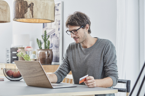 Mann hält eine Karte mit Laptop auf dem Tisch zu Hause, lizenzfreies Stockfoto