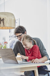 Lächelnder Vater und Tochter benutzen einen Laptop auf einem Tisch zu Hause - RORF01171
