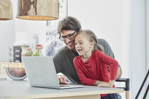 Glücklicher Vater und Tochter benutzen Laptop auf dem Tisch zu Hause, lizenzfreies Stockfoto