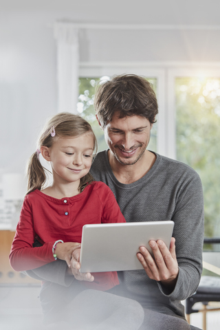 Lächelnder Vater und lächelnde Tochter verwenden gemeinsam ein Tablet zu Hause, lizenzfreies Stockfoto