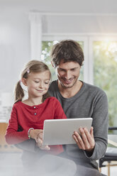 Lächelnder Vater und lächelnde Tochter verwenden gemeinsam ein Tablet zu Hause - RORF01180