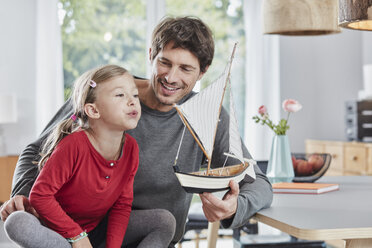 Happy father and daughter playing with model boat at home - RORF01183