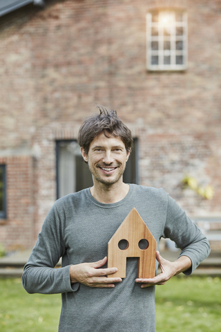 Porträt eines lächelnden Mannes vor seinem Haus mit Hausmodell, lizenzfreies Stockfoto