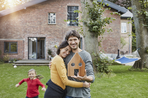 Porträt eines lächelnden Paares mit Tochter im Garten ihres Hauses mit Hausmodell, lizenzfreies Stockfoto