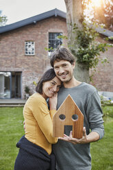 Porträt eines lächelnden Paares im Garten ihres Hauses mit Hausmodell - RORF01203