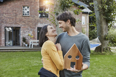 Glückliches Paar im Garten ihres Hauses mit Hausmodell - RORF01204