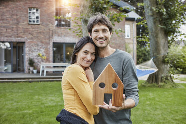 Porträt eines lächelnden Paares im Garten ihres Hauses mit Hausmodell - RORF01205