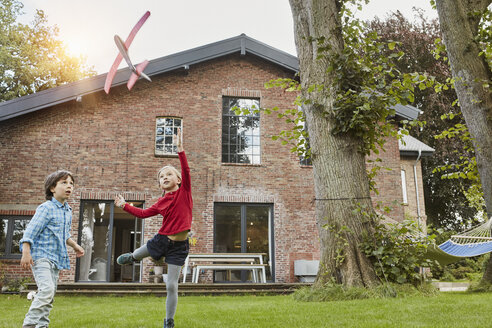 Zwei Kinder spielen mit einem Spielzeugflugzeug im Garten ihres Hauses - RORF01206