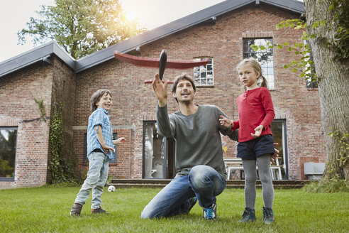 Vater mit zwei Kindern, die mit einem Spielzeugflugzeug im Garten ihres Hauses spielen - RORF01208