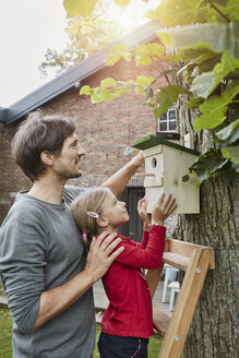 Vater und Tochter hängen Nistkasten im Garten auf - RORF01210