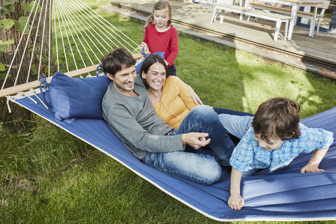 Glückliche Familie spielt in der Hängematte im Garten ihres Hauses, lizenzfreies Stockfoto