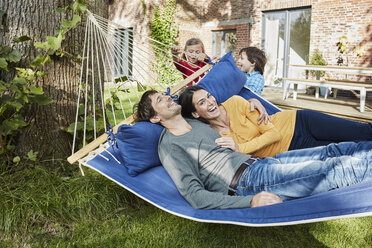 Happy family playing in hammock in garden of their home - RORF01216