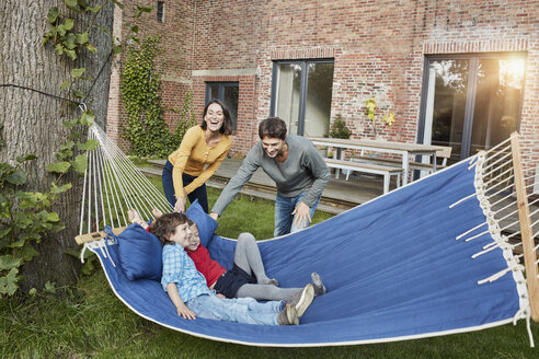 Happy family playing in hammock in garden of their home - RORF01217