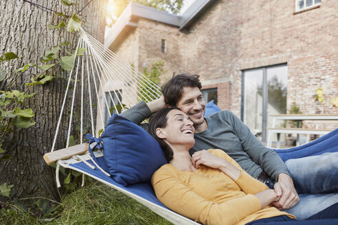Happy couple lying in hammock in garden of their home - RORF01218