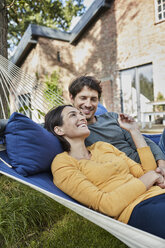 Ein glückliches Paar liegt in einer Hängematte im Garten seines Hauses - RORF01219