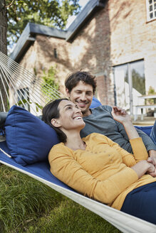 Happy couple lying in hammock in garden of their home - RORF01219
