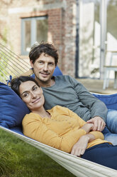 Smiling couple lying in hammock in garden of their home - RORF01220