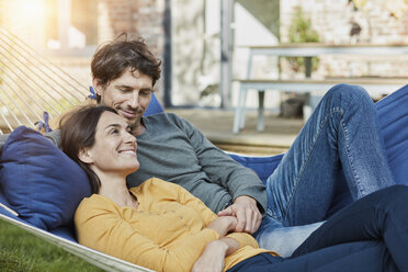 Smiling couple lying in hammock in garden of their home - RORF01221