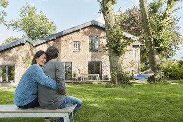 Lächelndes, liebevolles Paar, das im Garten seines Hauses sitzt - RORF01223